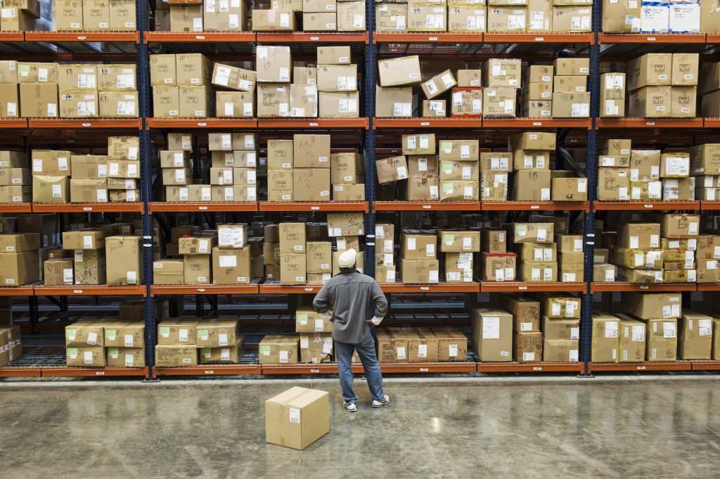 Warehouse worker checking inventory next to large racks of cardboard boxes holding product in a